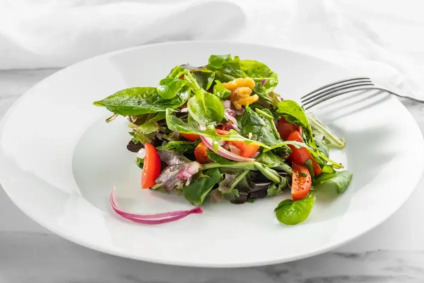 A plate of mixed greens salad with cherry tomatoes, red onion, and walnuts.