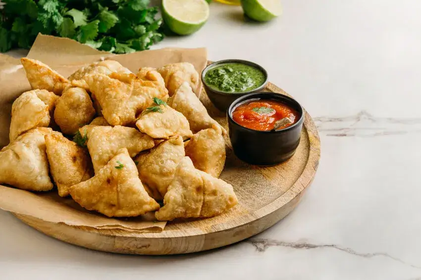 A plate of crispy samosas served with green chutney and red chili sauce