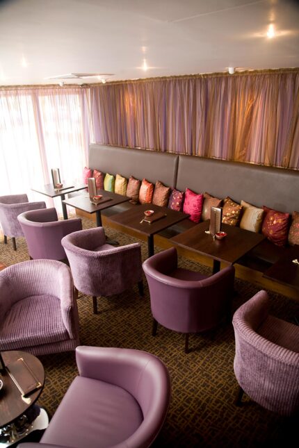 Comfortable purple chairs and booth seating with decorative cushions at Zari Crawley.