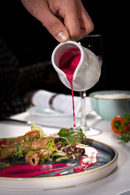 Pouring a vibrant pink beetroot sauce over grilled seekh kebabs at Zari Restaurant.