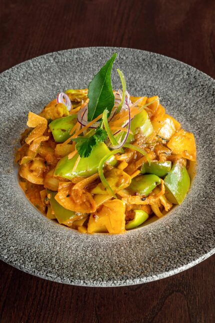 A vibrant vegetable curry dish garnished with fresh herbs and a curry leaf.
