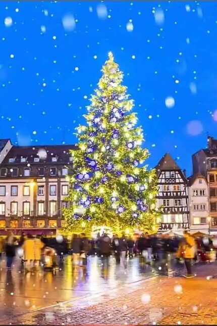A brightly lit holiday tree glowing with blue and yellow lights amidst winter snowfall.