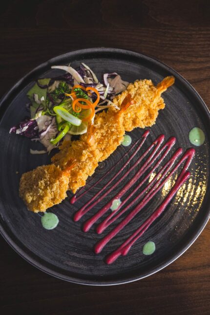 Crispy breaded king prawns with a fresh salad and artistic sauce drizzles for an Easter menu.