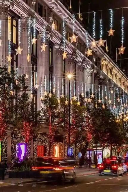 Festive holiday star lights hanging over a bustling city street during New Year's Eve.