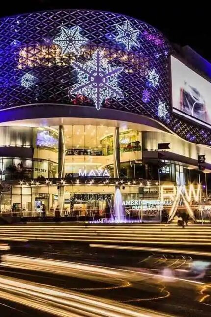 Modern shopping mall facade lit up with festive lights and traffic motion trails.