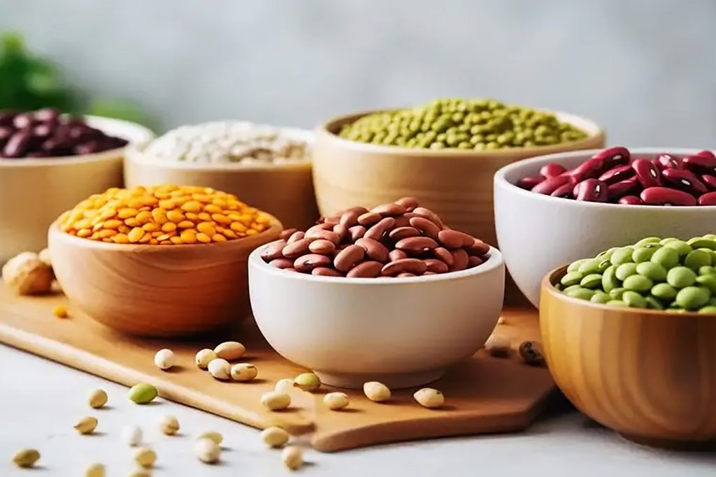 Bowls of protein-rich red kidney beans, green lentils, and split peas on a wooden board.