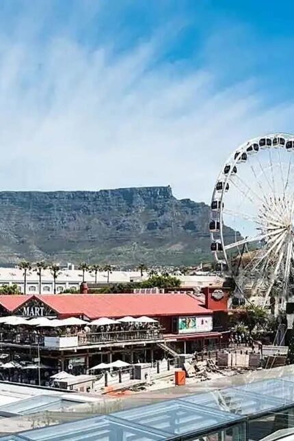 Scenic view of Table Mountain behind a bustling waterfront and white ferris wheel.