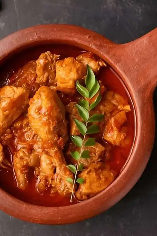 Spicy chicken Chettinad curry in a traditional pot garnished with fresh curry leaves.