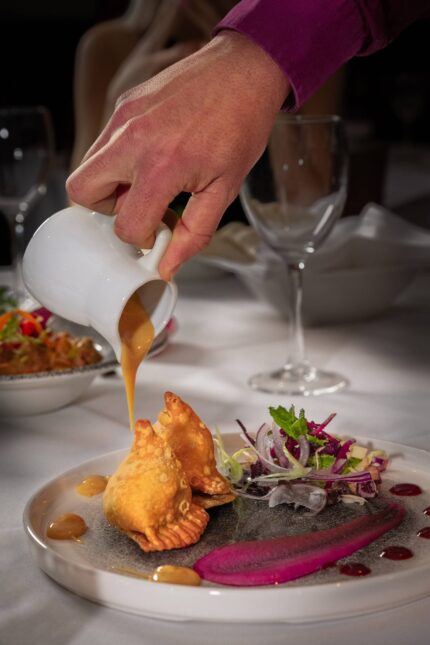 Crispy golden samosas being drizzled with sweet chutney next to a fresh side salad.