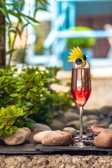 A festive pink champagne cocktail garnished with an apple fan in a bright garden setting.