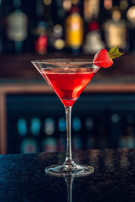 A vibrant red Christmas martini cocktail garnished with a fresh strawberry at the bar.