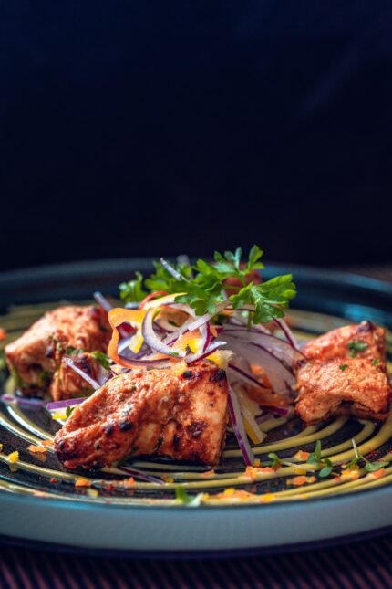 Sizzling tandoori chicken tikka pieces garnished with red onion rings and microgreens.