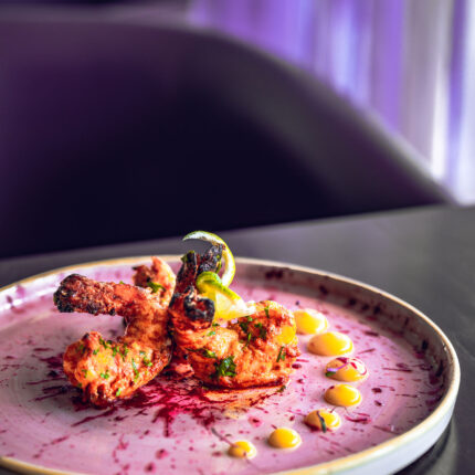 Gourmet tandoori king prawns elegantly arranged over a vibrant pink sauce signature swirl.