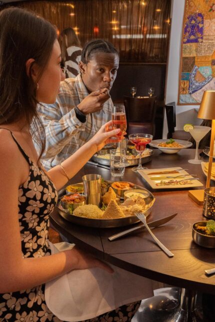 Diners sharing an authentic Indian thali platter and raising glasses at a festive party.