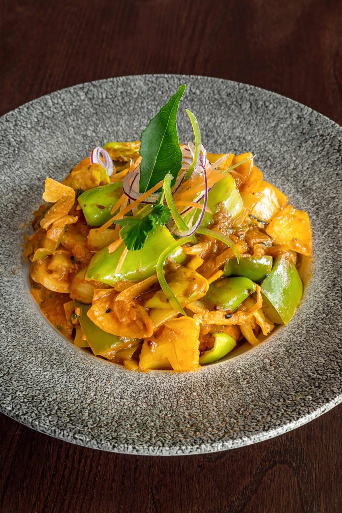 A vibrant vegetable curry dish garnished with fresh herbs and a curry leaf.