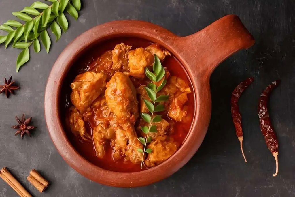 Spicy chicken Chettinad curry in a traditional pot garnished with fresh curry leaves.
