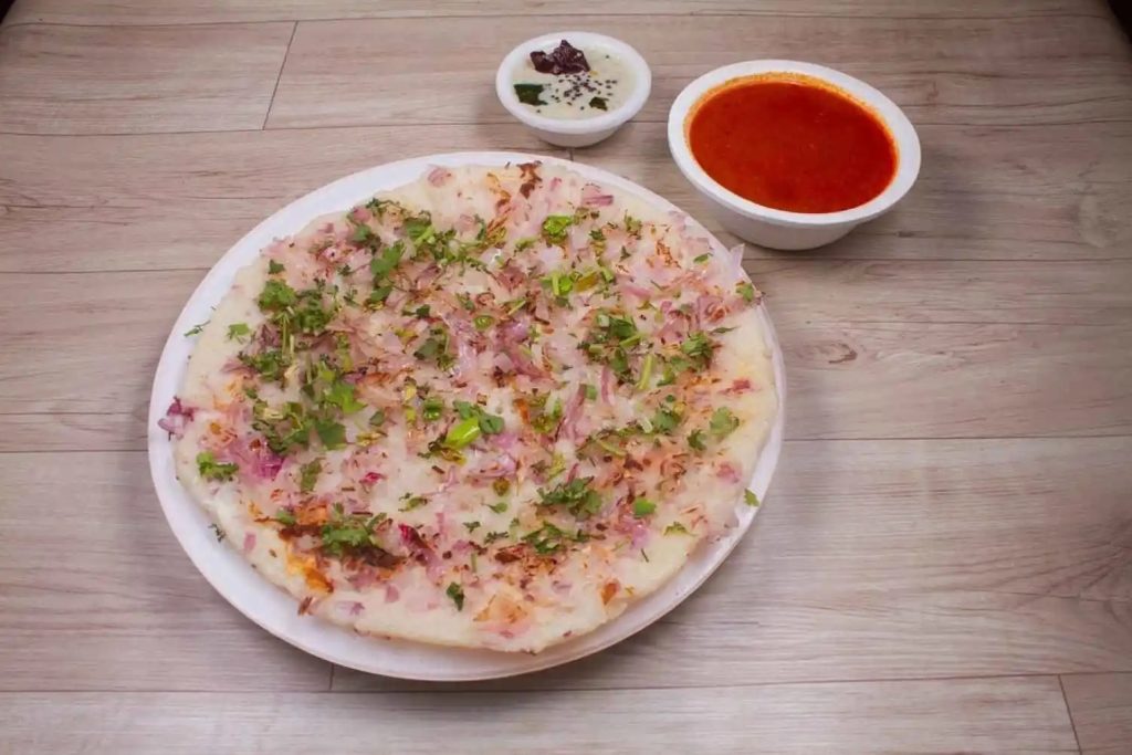 Thick South Indian uttapam pancake topped with onions and herbs, served with chutneys.