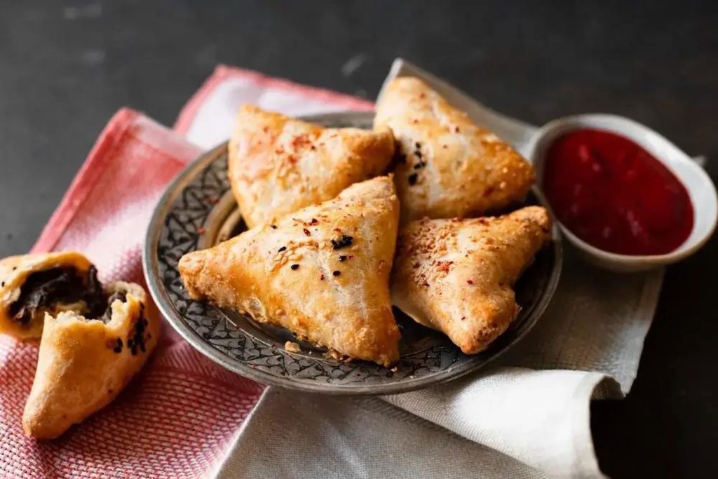 Three crispy golden samosas served fresh on a decorative plate at Zari Crawley.
